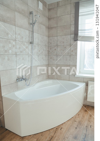 Corner acrylic bathtub with plastic front panel underneath in a bathroom with a window 131941047