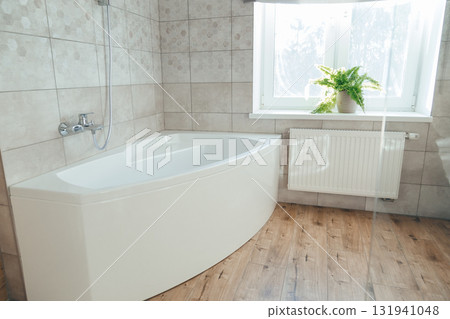 Corner acrylic bathtub with plastic front panel underneath in a bathroom with a window 131941048
