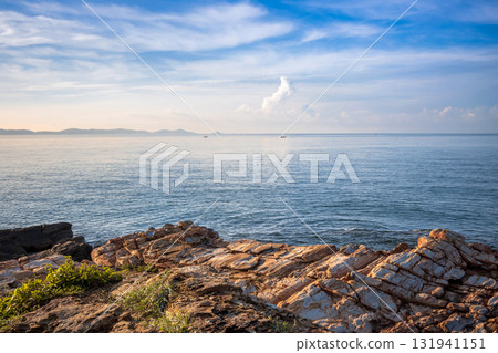 Striking coastal rock formations at Khao Laem Ya, Rayong, Thailand, contrasting with the calm blue ocean and wispy clouds under a bright summer sky Striking coastal rock formations at Khao Laem Ya, Rayong, Thailand, contrasting with the calm blue ocean and wispy clouds under a bright summer sky 131941151