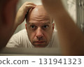 Concerned man examining bald head in bathroom mirror 131941323