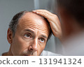 Worried man checking hair loss in mirror 131941324
