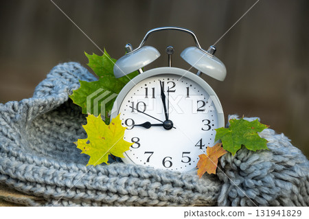Alarm clock with autumn leaves resting on a knitted scarf, time for fall season. 131941829