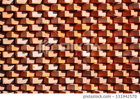 Stacked red clay bricks create a repeating textured wall with angular shadows. Urban materiality, geometric texture, construction elements, light and form Stacked red clay bricks create a repeating textured wall with angular shadows. Urban materiality, geometric texture, construction elements, light and form 131942570