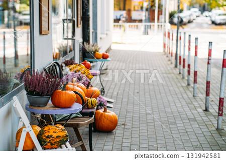 Colorful pumpkins and fall flowers decorate a sidewalk cafe exterior on a city street. Autumn decor ideas, urban seasonality, sidewalk charm, local business visibility 131942581