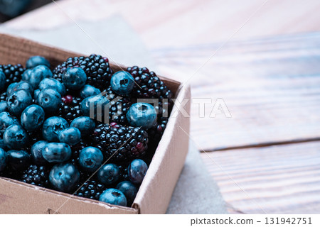 Blueberries and blackberries in a cardboard box on a wooden table Blueberries and blackberries in a cardboard box on a wooden table 131942751
