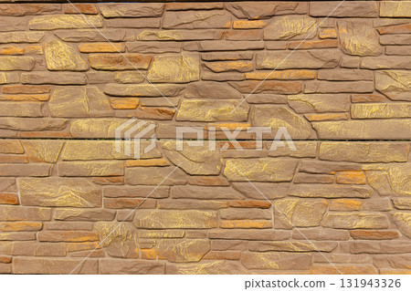 Textured close up of decorative stone fence built with horizontal layers of rectangular stones in beige and golden tones. Suitable for architecture, construction, and outdoor design backgrounds 131943326