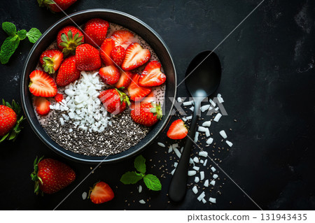 Smoothie bowl with chia seeds, coconut flakes and strawberries lying on dark background, decorated with mint leaves 131943435