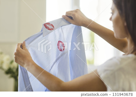 Woman stressed holding shirt with lipstick kiss marks symbolizing cheating and divorce 131943678
