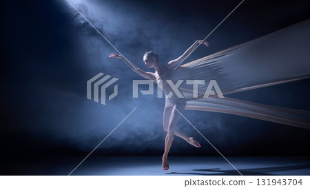 Ballet dancer in fabric performing elegant leap under blue haze light Ballet dancer in fabric performing elegant leap under blue haze light 131943704