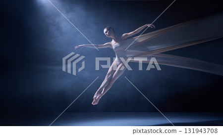 Ballet dancer leaping with fabric tied around body under blue light 131943708