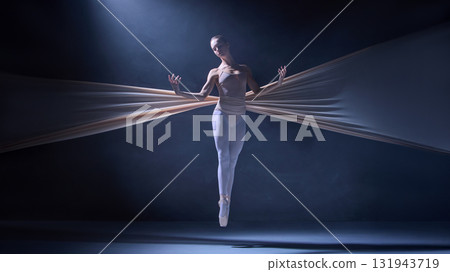 Ballet dancer suspended midair bound by stretched fabric under blue haze 131943719