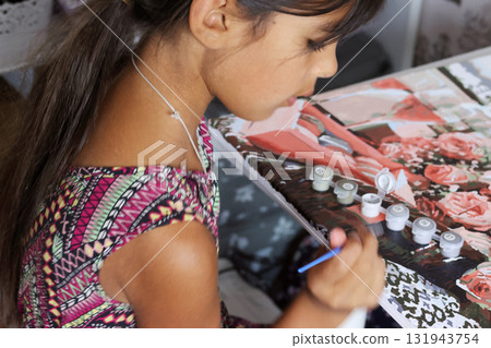A girl paints a picture using paints and a brush. Paint by numbers. Side Profile Shot 131943754