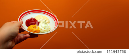 A captivating banner image featuring a hand holding a white plate with samples of various dipping sauces, ketchup, mustard, mayonnaise, garlic sauce. Copy space 131943768