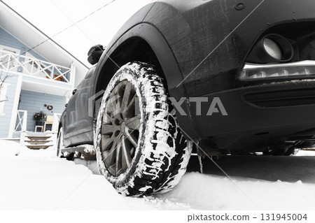 A black car sits on a snowy driveway, its tire coated with powdery snow 131945004