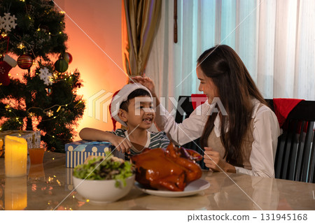 Loving mother touching her son's head while celebrating Christmas together at home. Warm family moment with gifts, festive dinner, and Christmas tree lights, expressing happiness, love, and 131945168