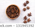 Star anise seeds in a wooden bowl on linen. Fruits of Illicium verum, also known as badian, Chinese star anise, star aniseed. Spice that closely resembles anise in flavor. Close-up, from above. Photo 131945392