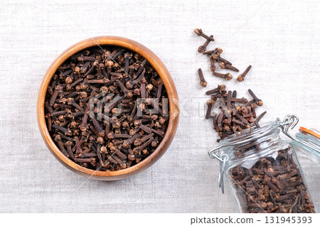 Dried cloves, in a wooden bowl, on linen. Aromatic flower buds of the tree Syzygium aromaticum, used as a spice, flavoring, or fragrance in cuisine, cosmetic products, etc. Close-up, from above. Photo Dried cloves, in a wooden bowl, on linen. Aromatic flower buds of the tree Syzygium aromaticum, used as a spice, flavoring, or fragrance in cuisine, cosmetic products, etc. Close-up, from above. Photo 131945393