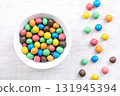 Colorful sugar-coated chocolate dragees, in a white bowl, on linen. Dragee chocolate confectionery, consisting of a multi colored candy shell, surrounding a chocolate filling. Close-up, from above. 131945394