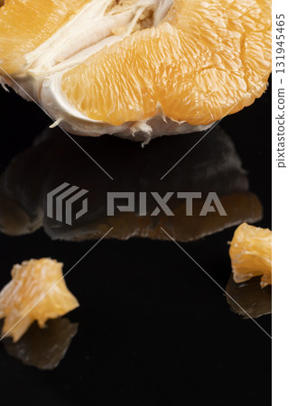 half of an citrus on a black mirror surface, ripe sweet and juicy citrus is reflected on the black surface 131945465
