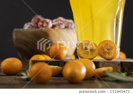 citrus-flavored orange juice and fresh kumquat fruits on a wooden table, fresh orange juice and fresh kumquat fruits next to a glass 131945471
