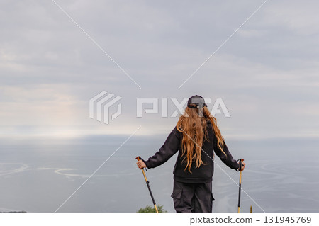 A woman with long hair stands on a hill overlooking the ocean A woman with long hair stands on a hill overlooking the ocean 131945769