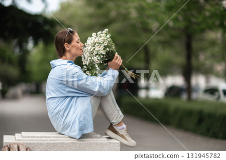 Daisies Bouquet Woman: Sits on bench in park, closes eyes, enjoys flowers scent in springtime daylight. Daisies Bouquet Woman: Sits on bench in park, closes eyes, enjoys flowers scent in springtime daylight. 131945782