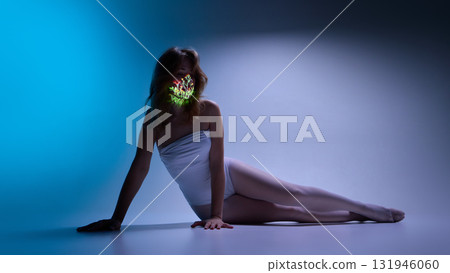 Woman in white bodysuit with floral light projection on face in blue minimalist studio 131946060
