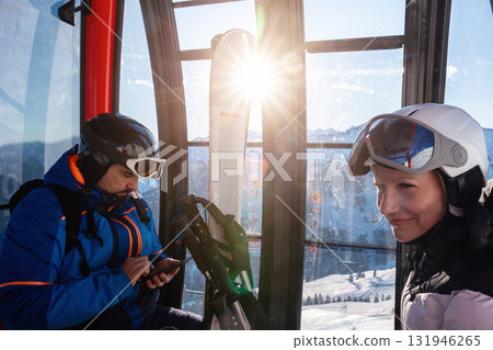 Scenic two skiers study trail map inside ski lift gondola at warm sunrise light at mountain alpine resort. Scenery group friends teamwork, planning, and excitement downhill winter sports adventure 131946265