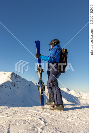 Skier stands on snowy mountain ridge facing bright horizon, ready for descent and challenge. Scene captures spirit of freedom, determination and strength in high alpine wilderness 131946266