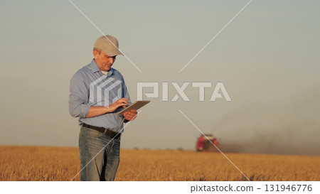 farmer working in wheat field, combine harvester ploughing in wheat field, agriculture tablet, farmer with a tablet in the field, harvesting wheat with a combine, digitally managing the harvest 131946776