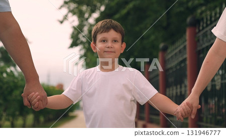 mother father holding child boy son hands, child smiling happiness, family walking together outdoors, parents provide support security, bond between them strong loving, child boy feels safe loved. 131946777