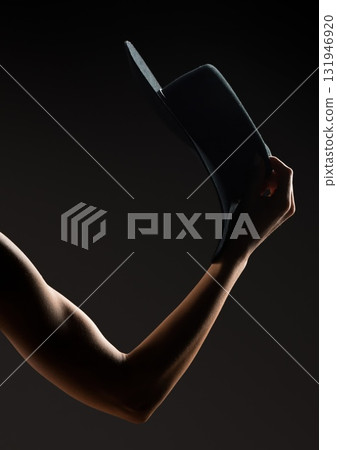 Hand gracefully holding a black hat against a dark background in a dramatic setting 131946920
