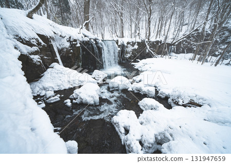 Snow-covered winter waterfall and silent forest 131947659