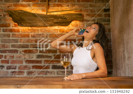 A woman relaxes with a glass of wine, engaged in a conversation on her phone in a rustic atmosphere. A woman relaxes with a glass of wine, engaged in a conversation on her phone in a rustic atmosphere. 131948292