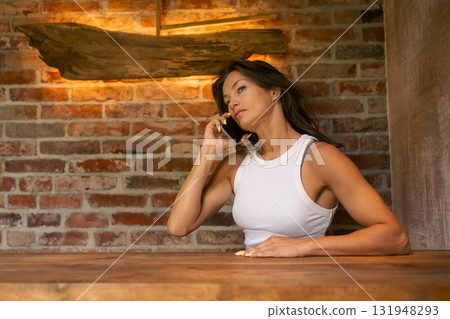 A woman is engaging in an important phone conversation while standing in front of a brick wall backdrop A woman is engaging in an important phone conversation while standing in front of a brick wall backdrop 131948293