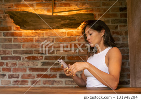 A woman uses her smartphone in a stylish, rustic brick setting that feels both inviting and contemporary A woman uses her smartphone in a stylish, rustic brick setting that feels both inviting and contemporary 131948294
