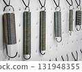 Metal springs of various sizes and finishes displayed on a wall for easy sorting and selection in a workshop setting 131948355