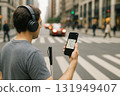 Man wearing headphones holding smartphone with navigation app, standing at city crosswalk 131949407