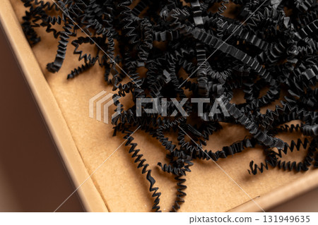 Postal cardboard box with shredded black paper filler close up Postal cardboard box with shredded black paper filler close up 131949635