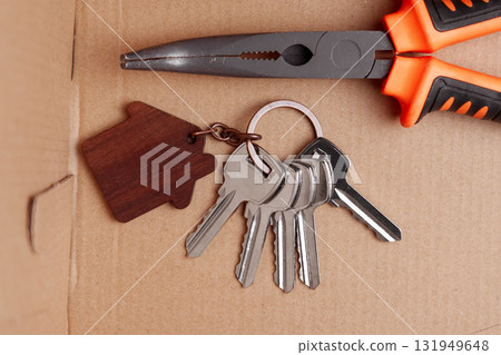 Door keys with wooden house-shaped keychain and construction tool in cardboard delivery box 131949648