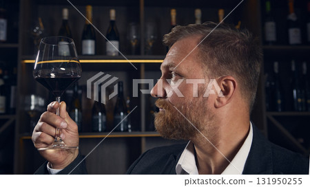 Sommelier examining color of wine in glass under warm light 131950255