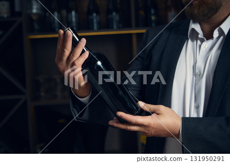 Sommelier examining wine bottle with focused expression Sommelier examining wine bottle with focused expression 131950291