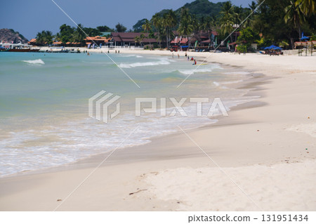 Bright sandy beach with gentle waves and people enjoying the sun in a tropical paradise during a clear summer day 131951434