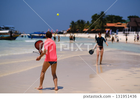 People playing beach tennis on a sunny day on a tropical beach with clear water and palm trees in the background. Redang Island. Malaysia People playing beach tennis on a sunny day on a tropical beach with clear water and palm trees in the background. Redang Island. Malaysia 131951436