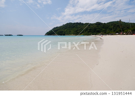 Tropical beach with clear water and soft sand at a tranquil coastal location under a bright blue sky 131951444