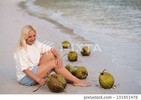 A girl is sitting on a tropical beach with coconuts in the morning enjoying the sunrise on Redang Island. Malaysia A girl is sitting on a tropical beach with coconuts in the morning enjoying the sunrise on Redang Island. Malaysia 131951478