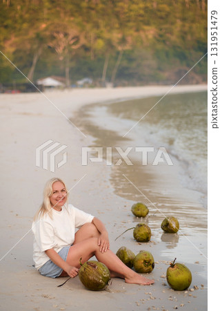 A woman enjoys a tropical beach, sitting next to fresh coconuts on a quiet coastline at dawn. Redang Island. Malaysia A woman enjoys a tropical beach, sitting next to fresh coconuts on a quiet coastline at dawn. Redang Island. Malaysia 131951479