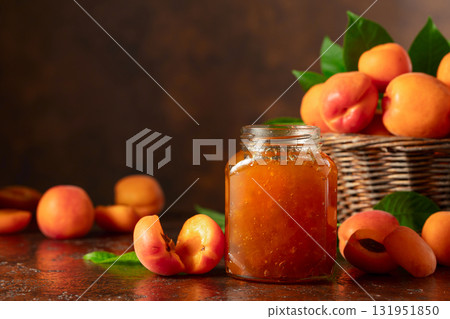 Apricot jam in jar and fresh fruits on a brown table. 131951850