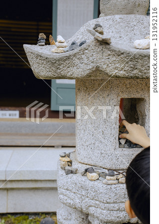 A child's hand stacking stones on a stone statue to make a wish. A child's hand stacking stones on a stone statue to make a wish. 131952116