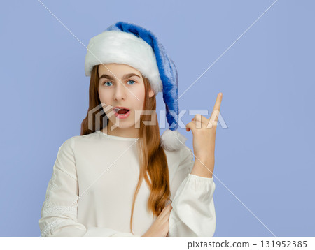 Smiling girl with blue Santa hat pointing up on blue background. Smiling girl with blue Santa hat pointing up on blue background. 131952385